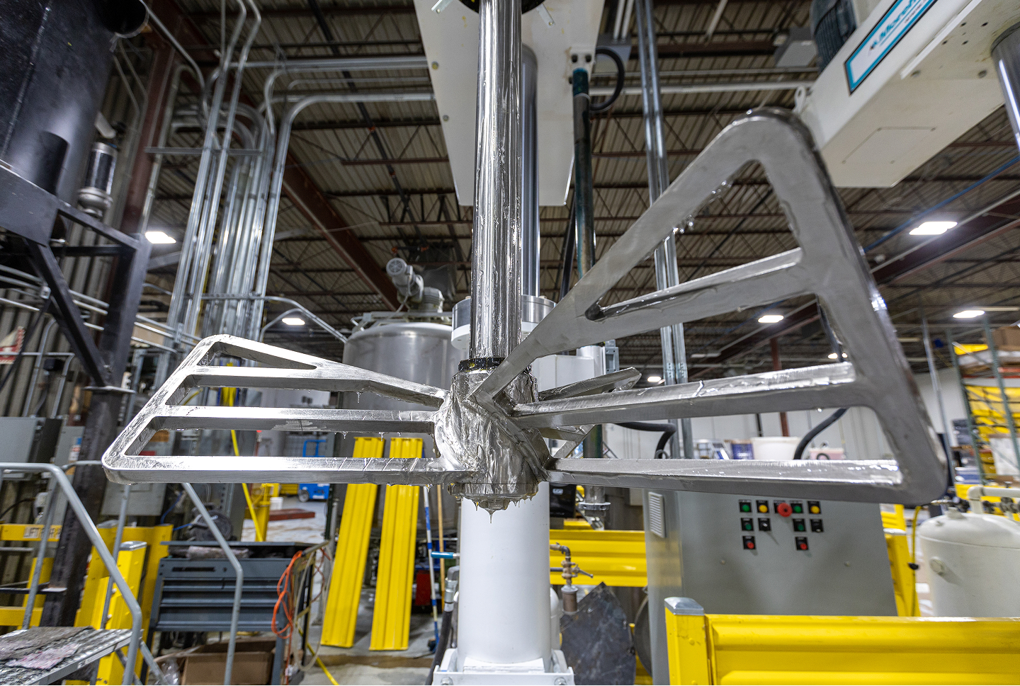 Industrial mixer blade in a factory, silver metal with yellow barriers in the background.