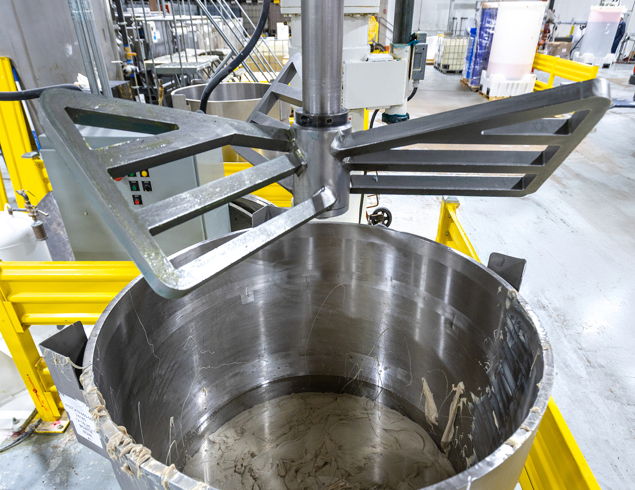 Industrial mixer in a factory with yellow railings and control panel, producing lubricant.