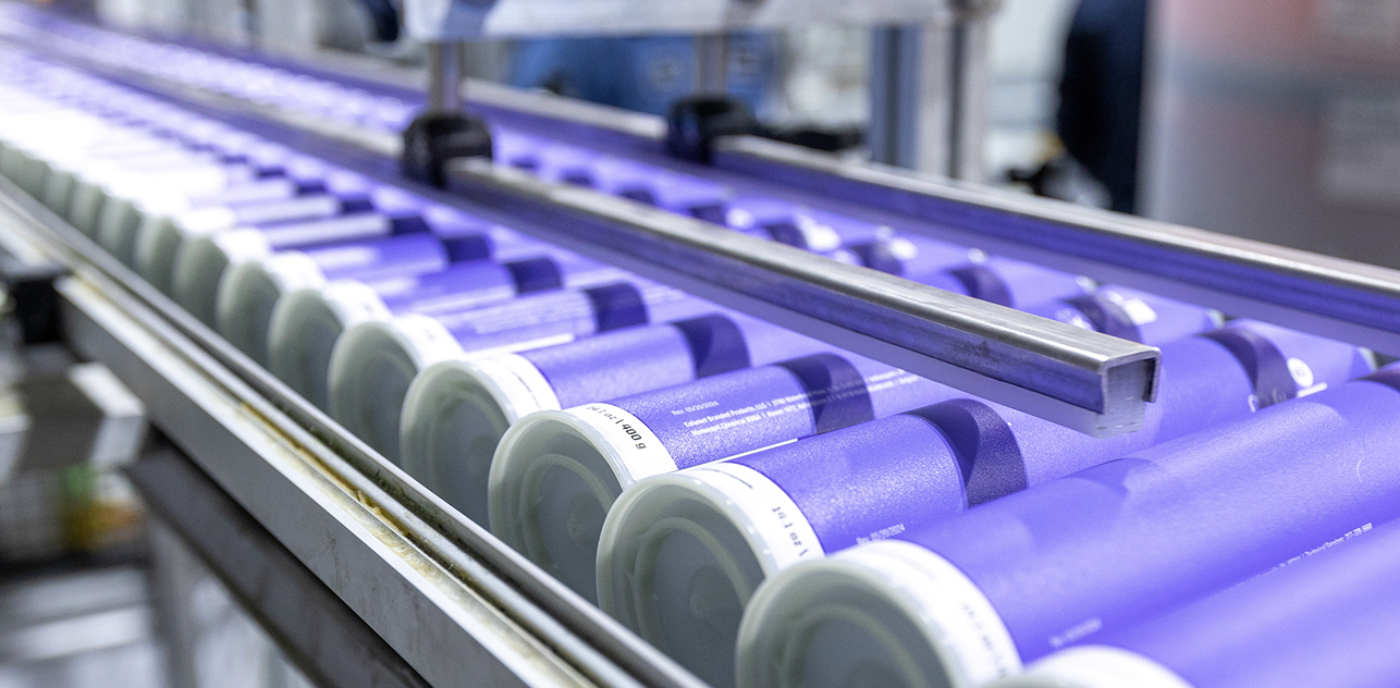 Purple cylinders with private labels on a conveyor in a manufacturing facility.