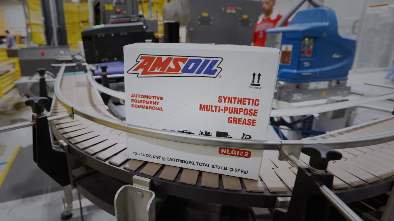 Box labeled "AMSOIL Synthetic Multi-Purpose Grease" on a conveyor belt.