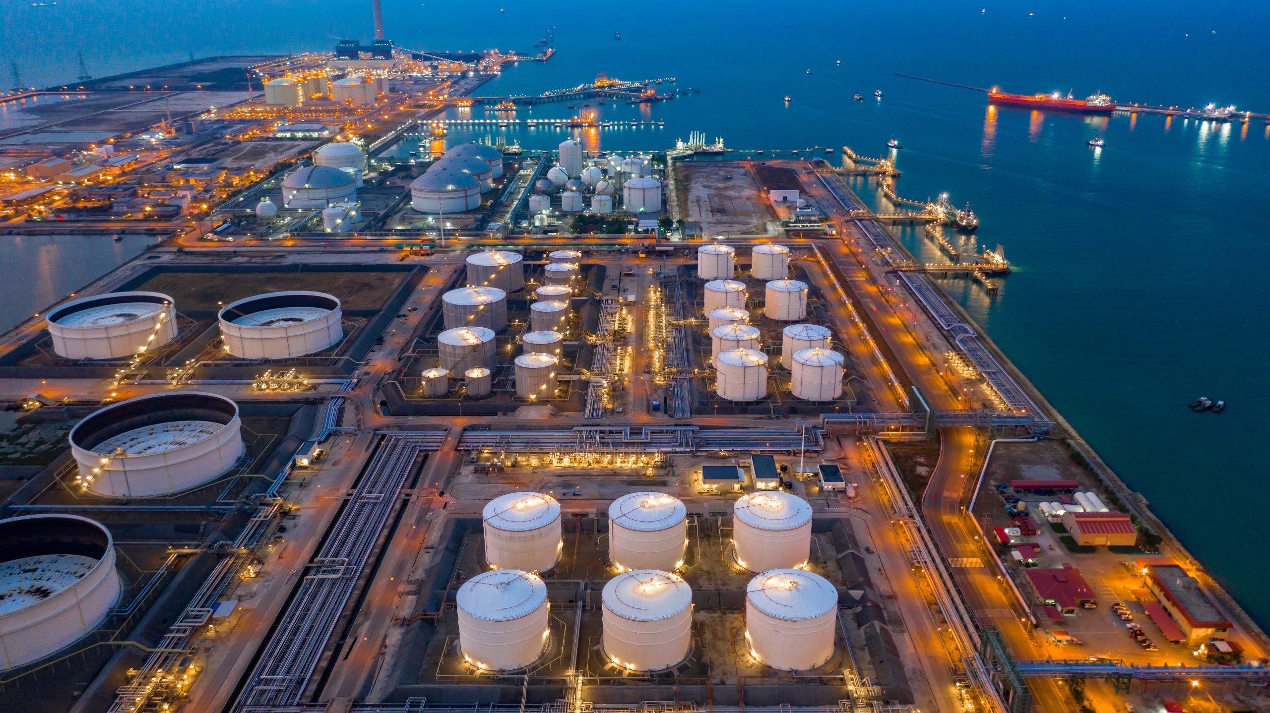 Aerial view of illuminated oil and gas terminal at night, near a body of water.