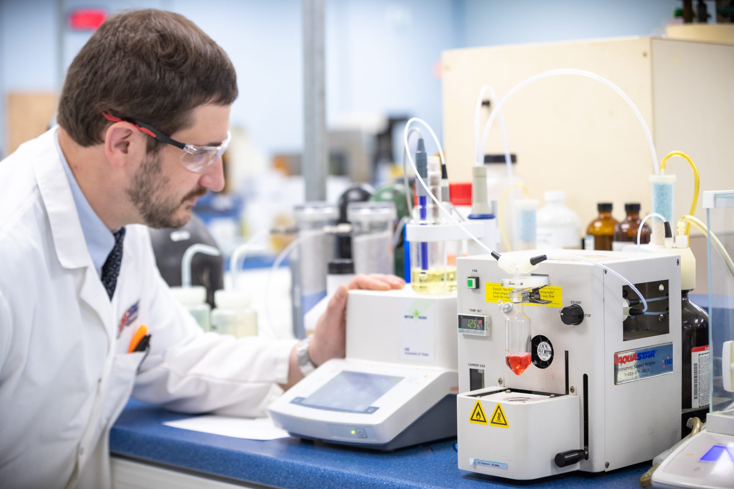 Lab technician in white coat operates equipment marked "AQUASTAR" on blue counter.