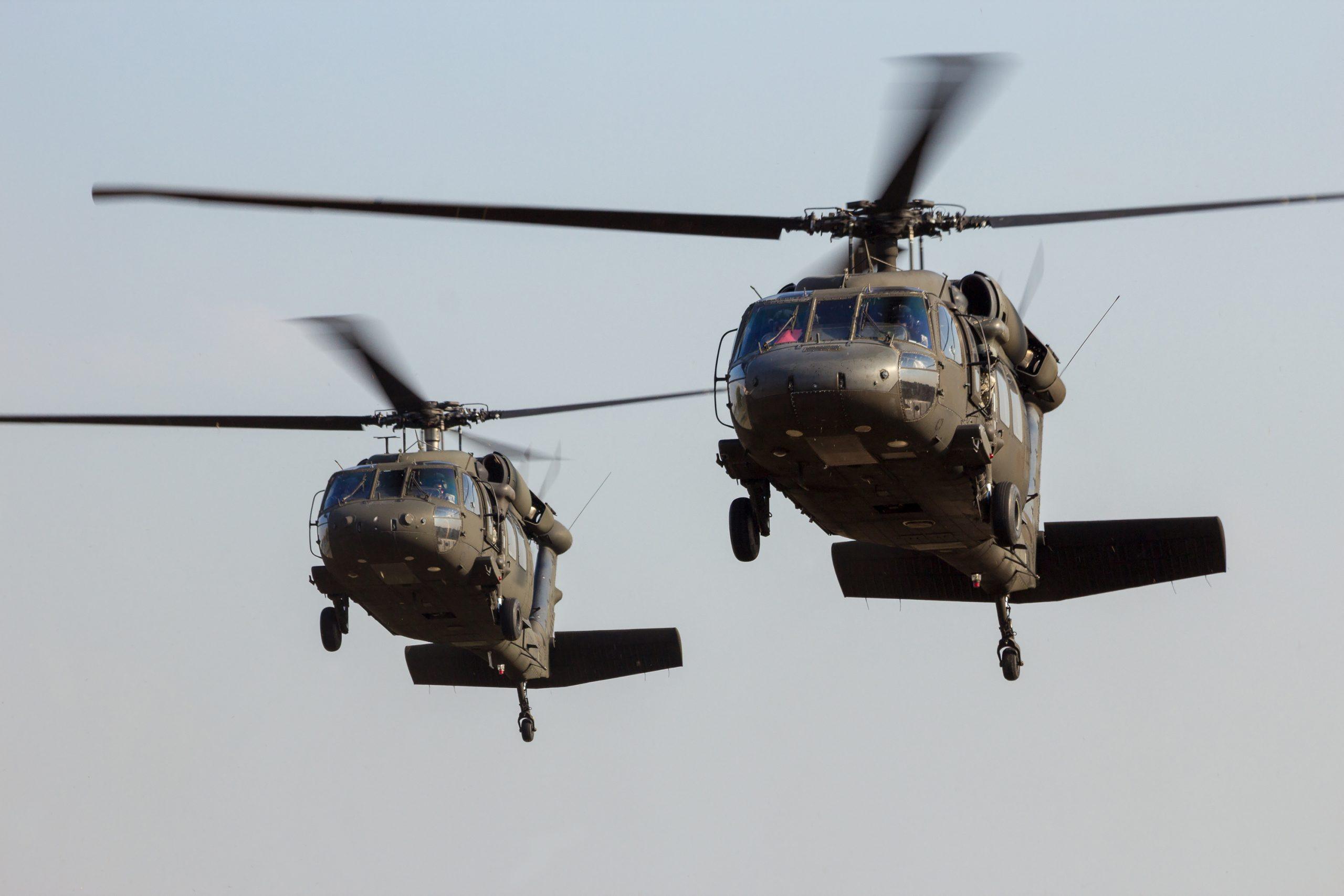 Two black helicopters flying in the sky against a light blue backdrop.