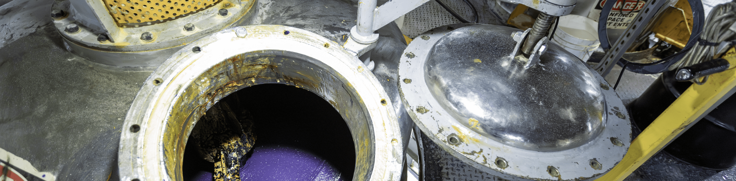 Open industrial machinery with visible purple lubricant inside. Silver cover nearby.